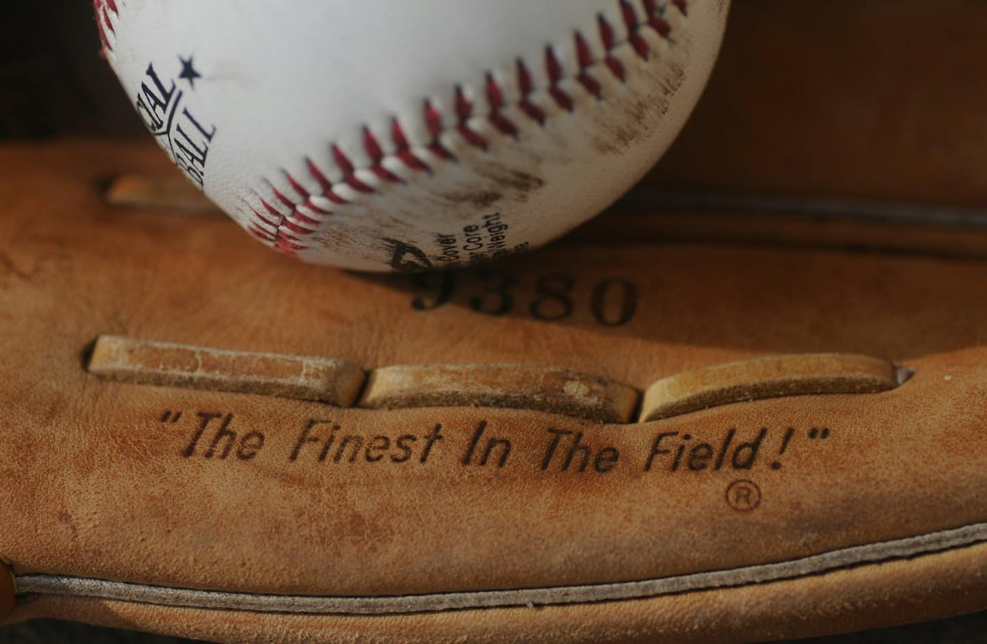 Una pallina da baseball appoggiata su un guanto di cuoio usurato.